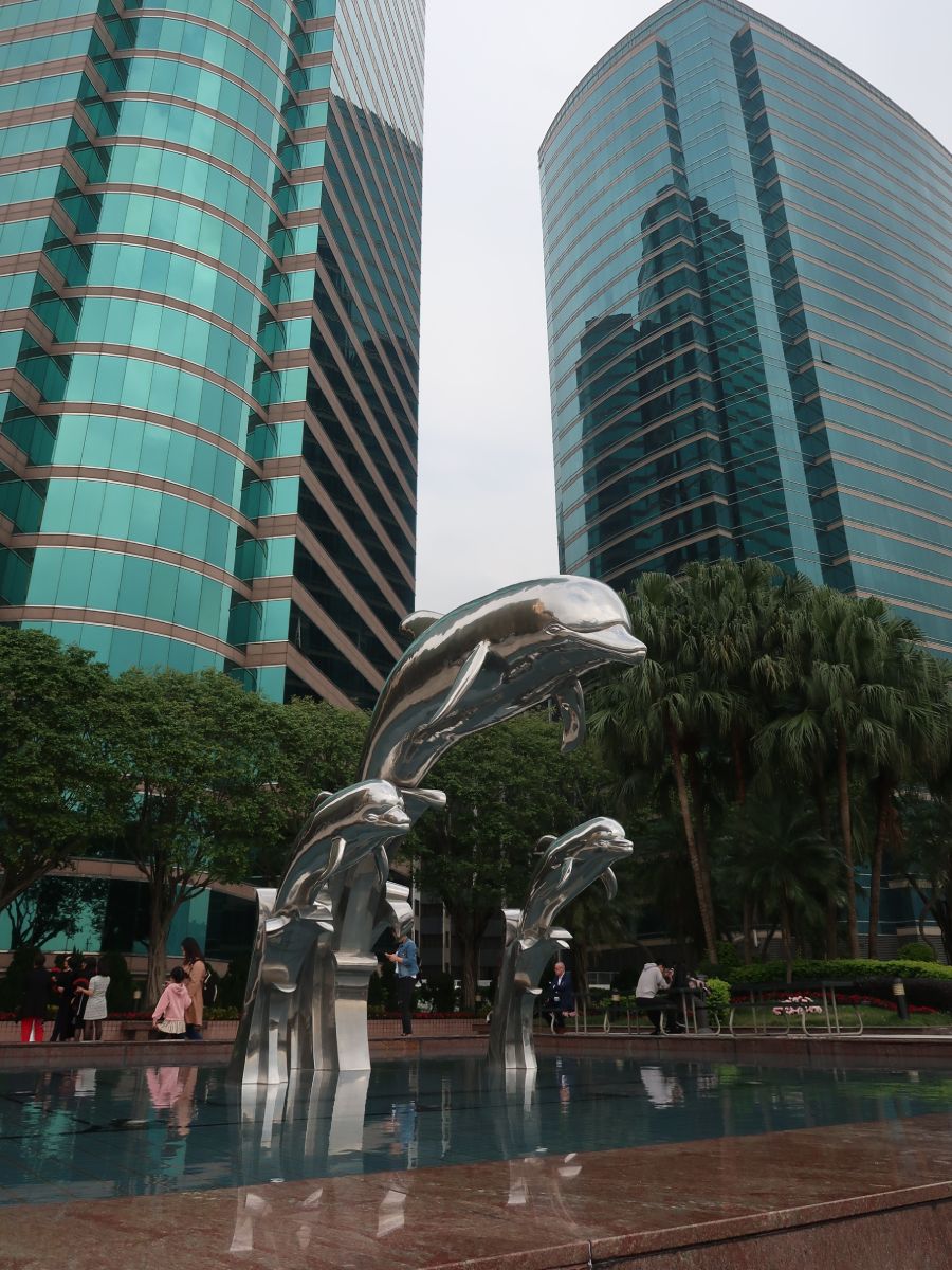 statues of silver dolphins in front of the skyscrapers