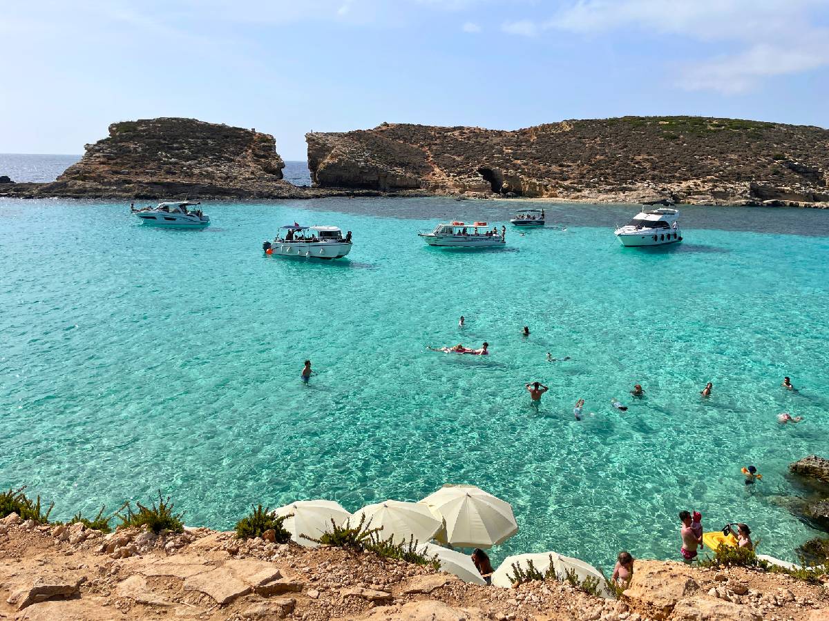 few people swimming and few small boats are parked in a crystal clear water in Blue Lagoon