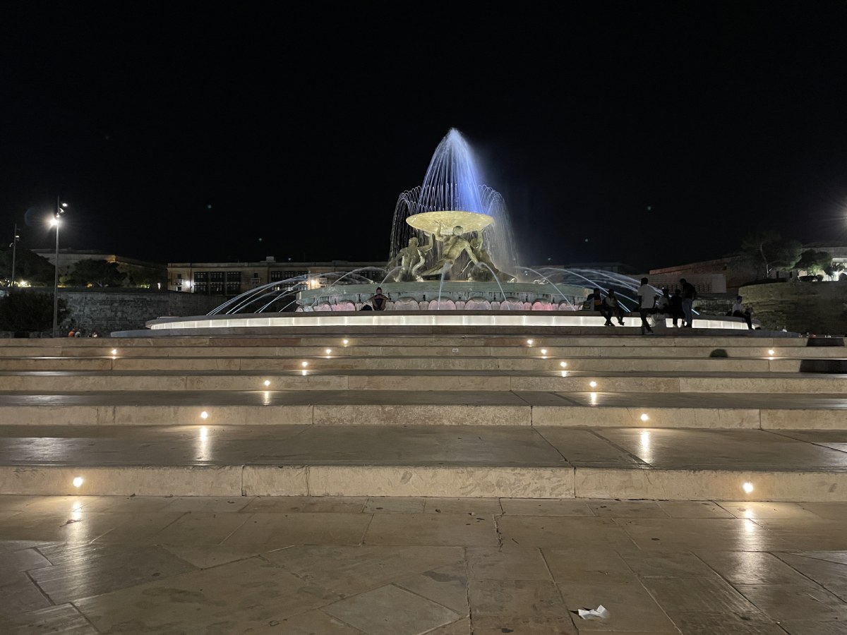 Night picture of the Triton fountain with lights on and few people resting next to the fountain